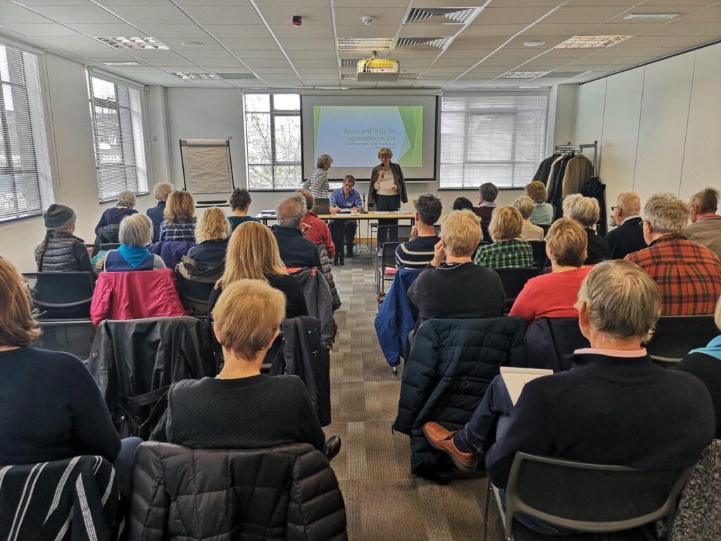 Members of Camphill Families and Friends at one of the group's Open Meetings. People are sat in rows facing the speakers at the front of the room,