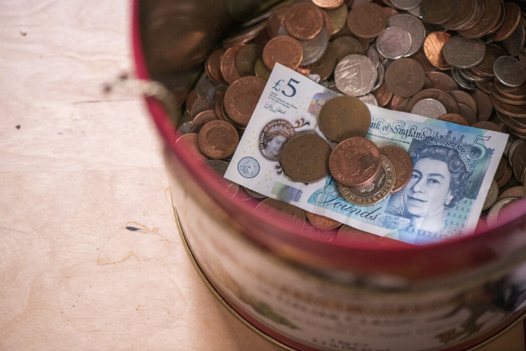 A tin containng lots of British coins and a five pound note